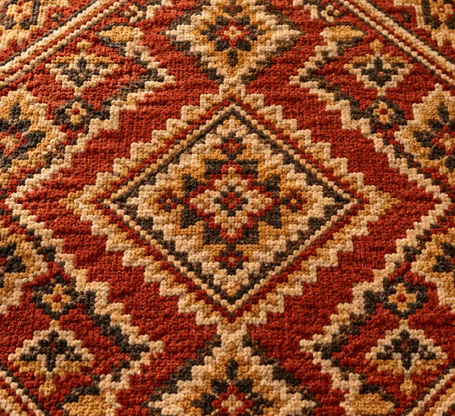 Close-up of a hand-knotted Indian carpet medallion in terracotta, ivory and gold, showing the knotted pile