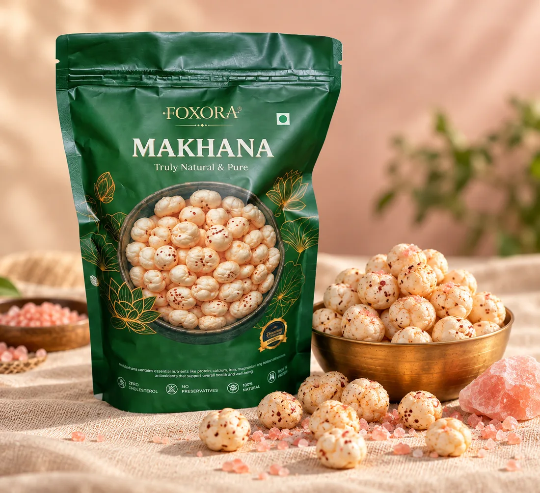 A green Foxora makhana pack beside a brass bowl of makhana and pink Himalayan salt crystals